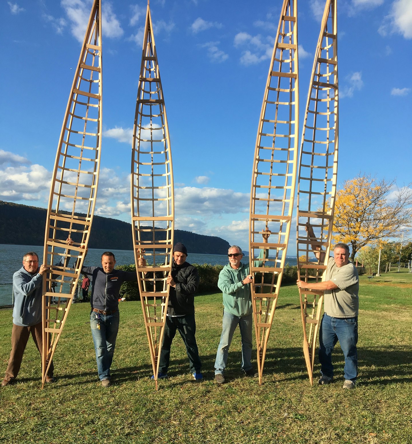 Four men holding kayak frames while building boats