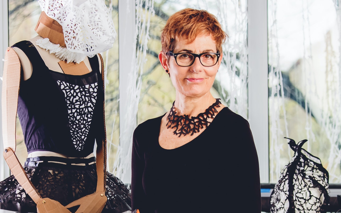 Visual artist Beatrice Coron posing with and wearing her cut creations. Photo by Ric Kallaher.